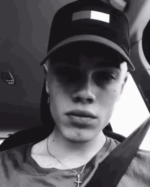 a black and white photo of a man wearing a hat and a cross necklace