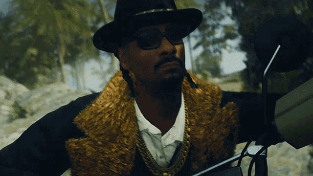 a man wearing a hat and sunglasses is standing next to a motorcycle