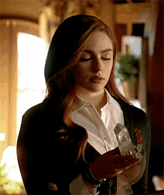 a woman in a black jacket and white shirt is holding a crystal in her hands .