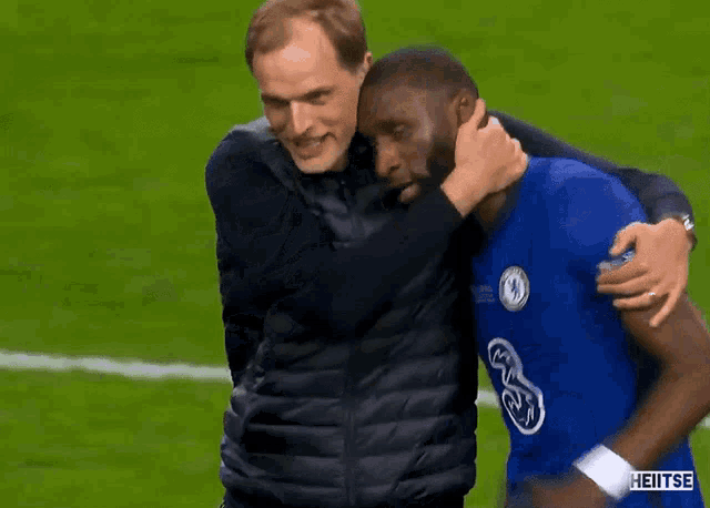 two men are hugging each other on a soccer field and one of them is wearing a chelsea shirt