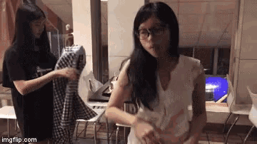 a girl wearing glasses is standing next to another girl holding a plaid shirt