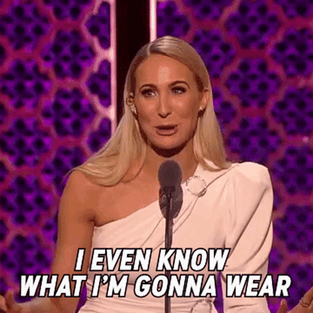 a woman in a white dress is speaking into a microphone and saying `` i even know what i 'm gonna wear ''
