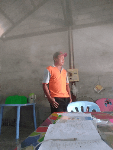 a man in an orange shirt stands in front of a table with papers on it