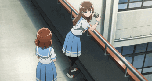 a girl taking a picture of another girl standing on a railing