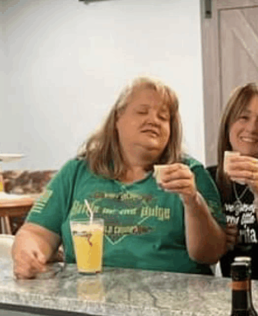 a woman in a green shirt is sitting at a bar holding a glass of orange juice .