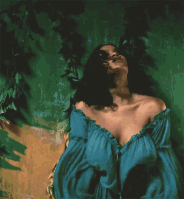 a woman in a blue off the shoulder top is standing in front of a green background .