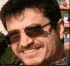 a man wearing sunglasses is smiling in a blurry photo .