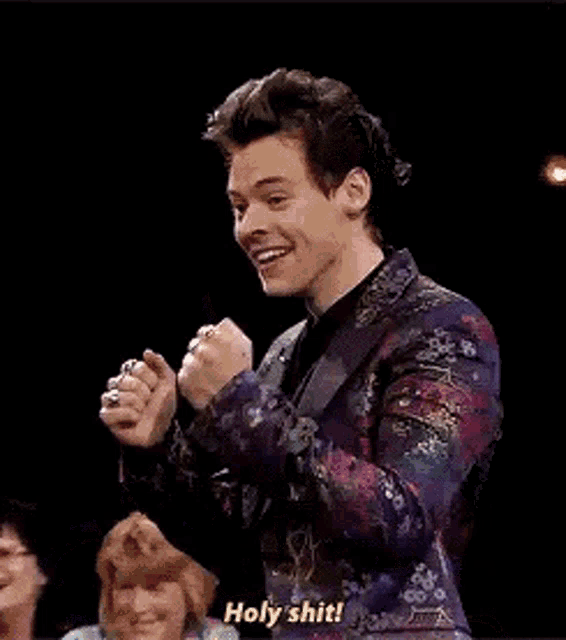 harry styles is wearing a floral suit and making a funny face while talking .