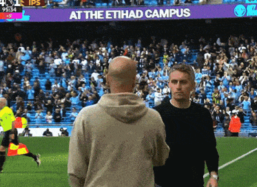 two men are standing on a soccer field in front of a sign that says at the etihad campus