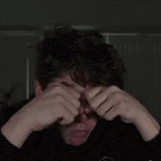 a man with curly hair is covering his face with his hands .