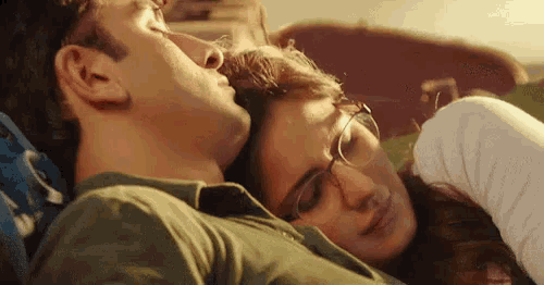 a man and a woman are laying on a bed . the woman is wearing glasses and the man is kissing her .