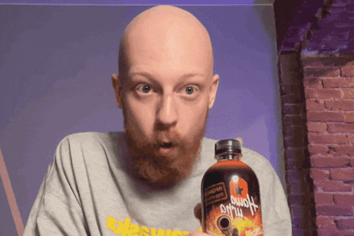 a bald man with a beard is holding a bottle of hot sauce that says ' aloha ' on it