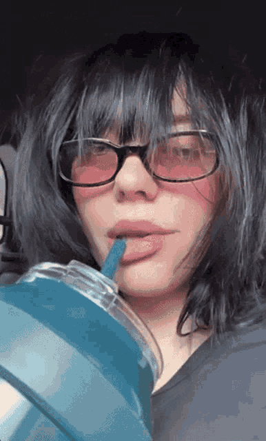 a woman wearing glasses is drinking from a cup with a straw .