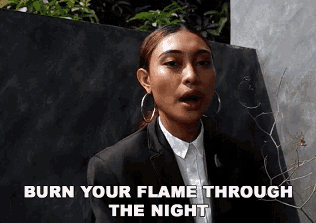a woman in a suit and hoop earrings is saying burn your flame through the night