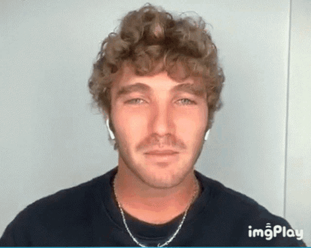 a man with curly hair and a mustache is wearing headphones and a black shirt .