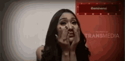 a woman is covering her mouth with her hands while standing in front of a red sign .