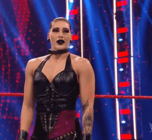 a woman is standing in a wrestling ring wearing a black top and a choker .