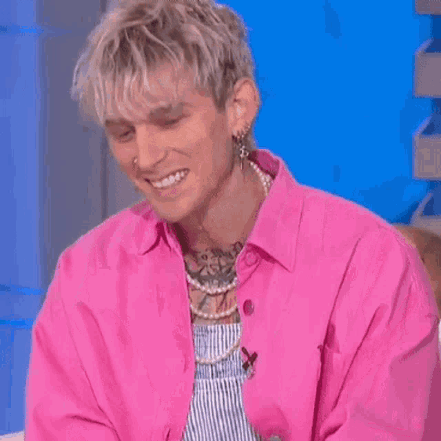 a man wearing a pink shirt and earrings is sitting on a couch .