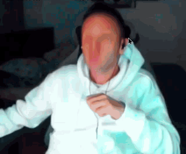 a man in a white hoodie is dancing in front of a computer monitor