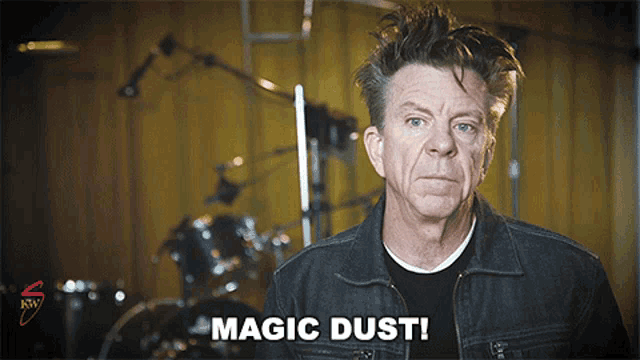 a man in a denim jacket says magic dust in front of a drum set