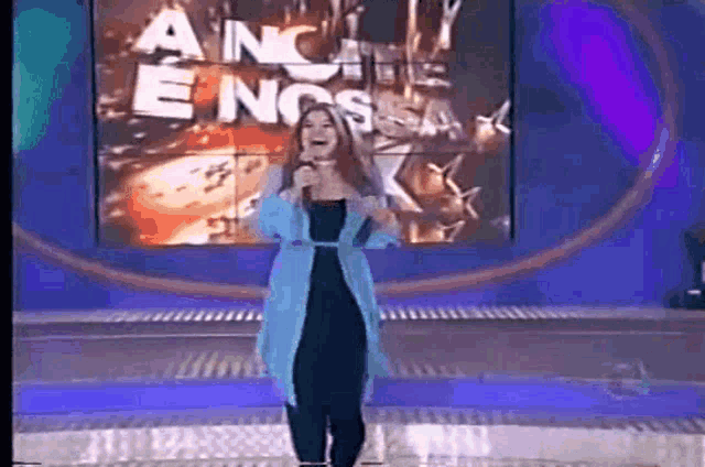 a woman is singing into a microphone on a stage in front of a screen that says " ancie e nossa " .