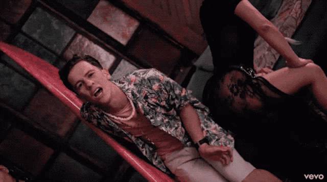 a man sitting on a couch next to two women with vevo on the bottom right