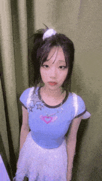 a young girl wearing a blue shirt and a white skirt is standing in front of a curtain .