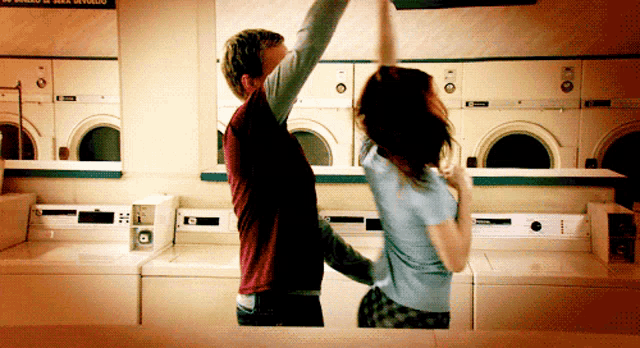 a man and a woman are dancing in a laundromat with a sign above them that says no smoking