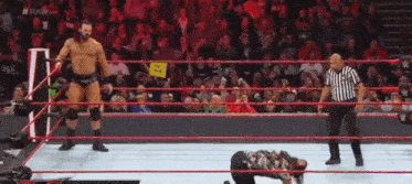 a referee is standing in a wrestling ring while a wrestler is kneeling on the ground .