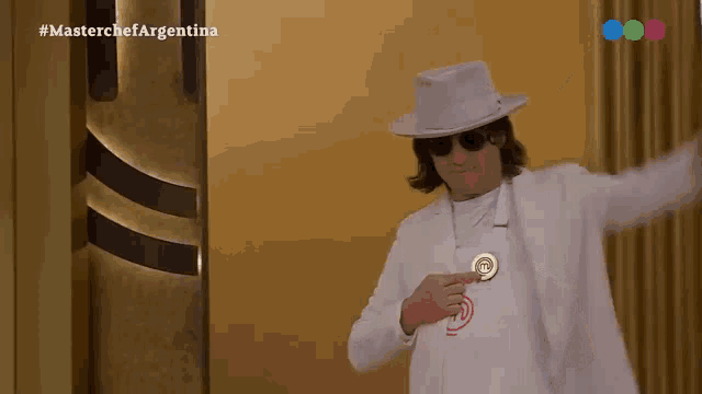 a man wearing a white hat and sunglasses is holding a medal in front of a wall that says masterchef argentina