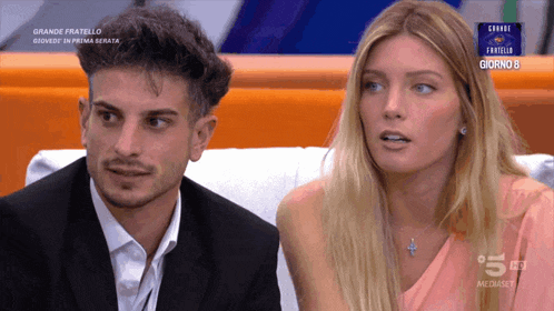 a man and a woman sit on a couch in front of a screen that says grande fratello
