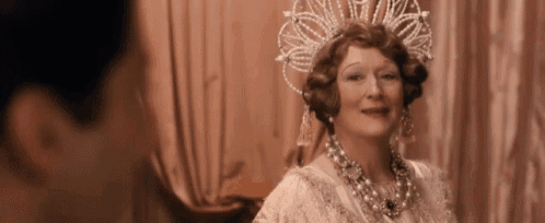 a woman wearing a tiara and a necklace is smiling while looking at a man .
