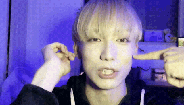 a young man with blonde hair is covering his ears with his fingers