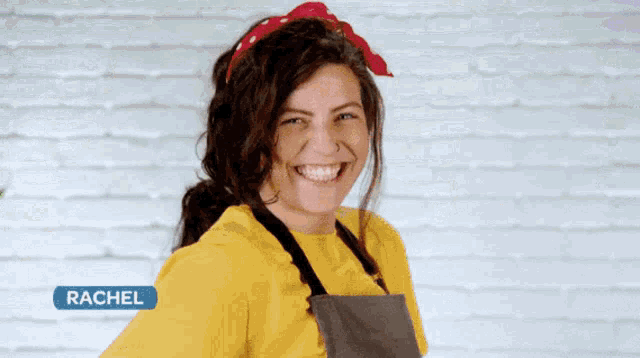 a woman wearing a yellow shirt and apron is standing in front of a brick wall
