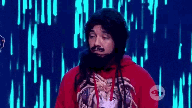 a man with long hair and a beard is wearing a red hoodie with a lion on it .
