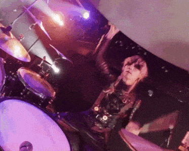 a person playing a drum set with purple lights behind them