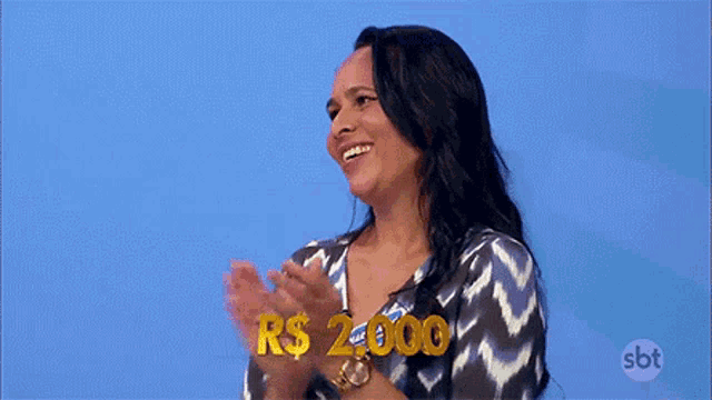 a woman is clapping her hands in front of a blue background while holding a sign that says r $ 2.000 .