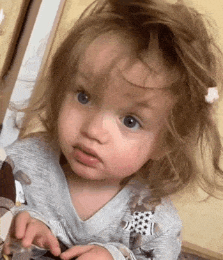 a baby girl with a messy hairdo is looking at the camera .
