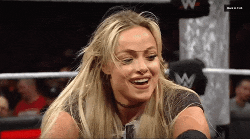 a woman is smiling in a wrestling ring with a sign that says back in 1:48