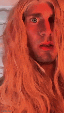 a man with long blonde hair and blue eyes makes a surprised face