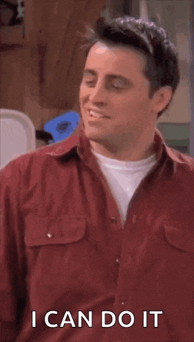 a man in a red shirt is smiling and saying `` i can do it '' while standing in a room .