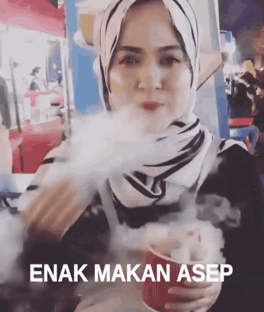 a woman in a hijab is smoking a cigarette and the words enak makan asep are on the bottom