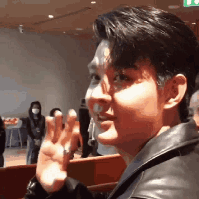 a man in a leather jacket is waving his hand in a crowd .