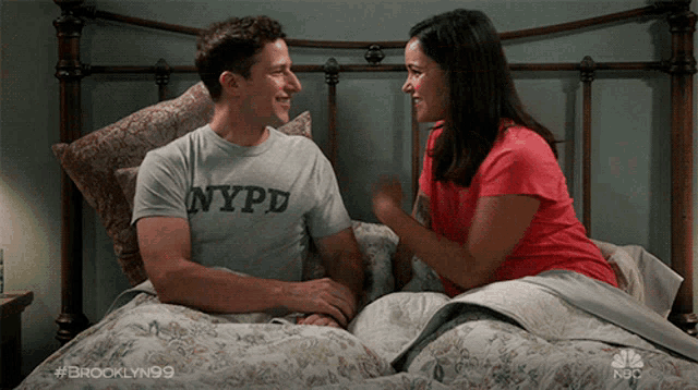 a man is wearing a nypd shirt while laying in bed with a woman