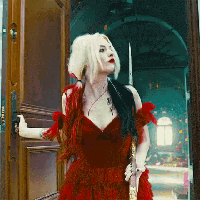a woman in a red dress is standing in a doorway holding a sword .