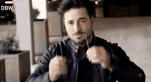 a man wearing a leather jacket is holding a pair of glasses in his hands .