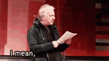 a man in a black jacket is holding a piece of paper and says `` i mean '' .