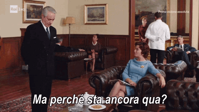 a man in a suit and tie stands next to a woman sitting in a chair with the words ma perche sta ancora qua below her