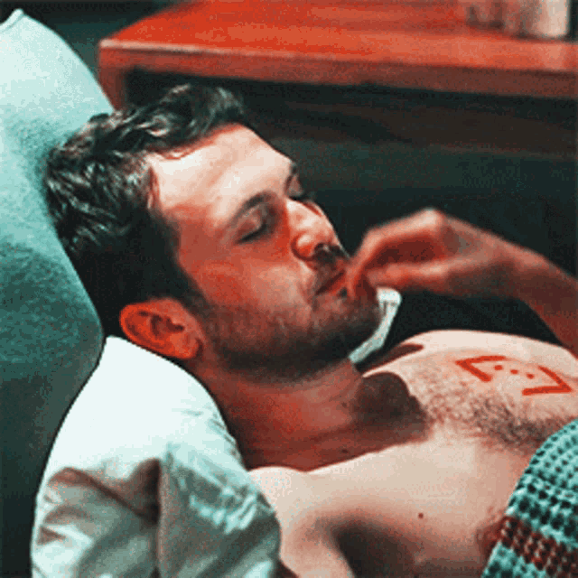a shirtless man is laying in a bed with a red x on his chest ..