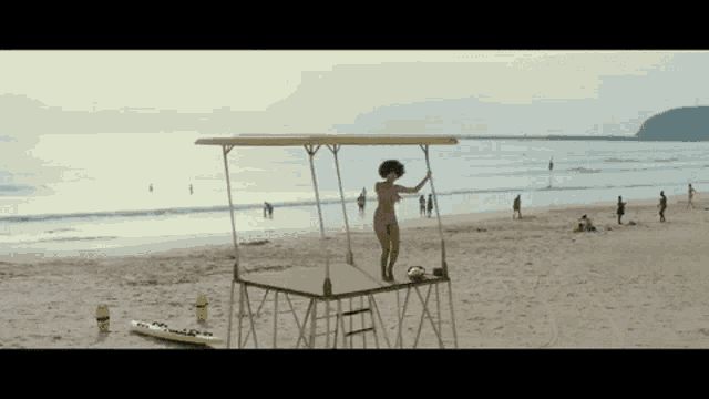 a naked woman stands on top of a lifeguard tower on the beach